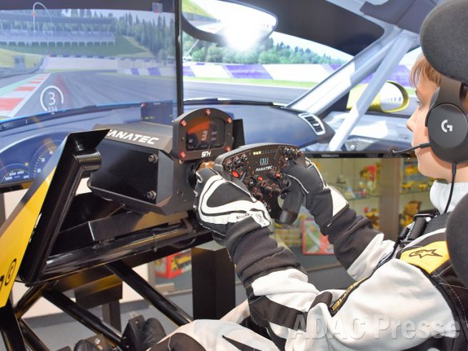 junge sitzt in full motion simulator vor monitoren in einem rennsitz und fährt virtuelles rennen im simracing